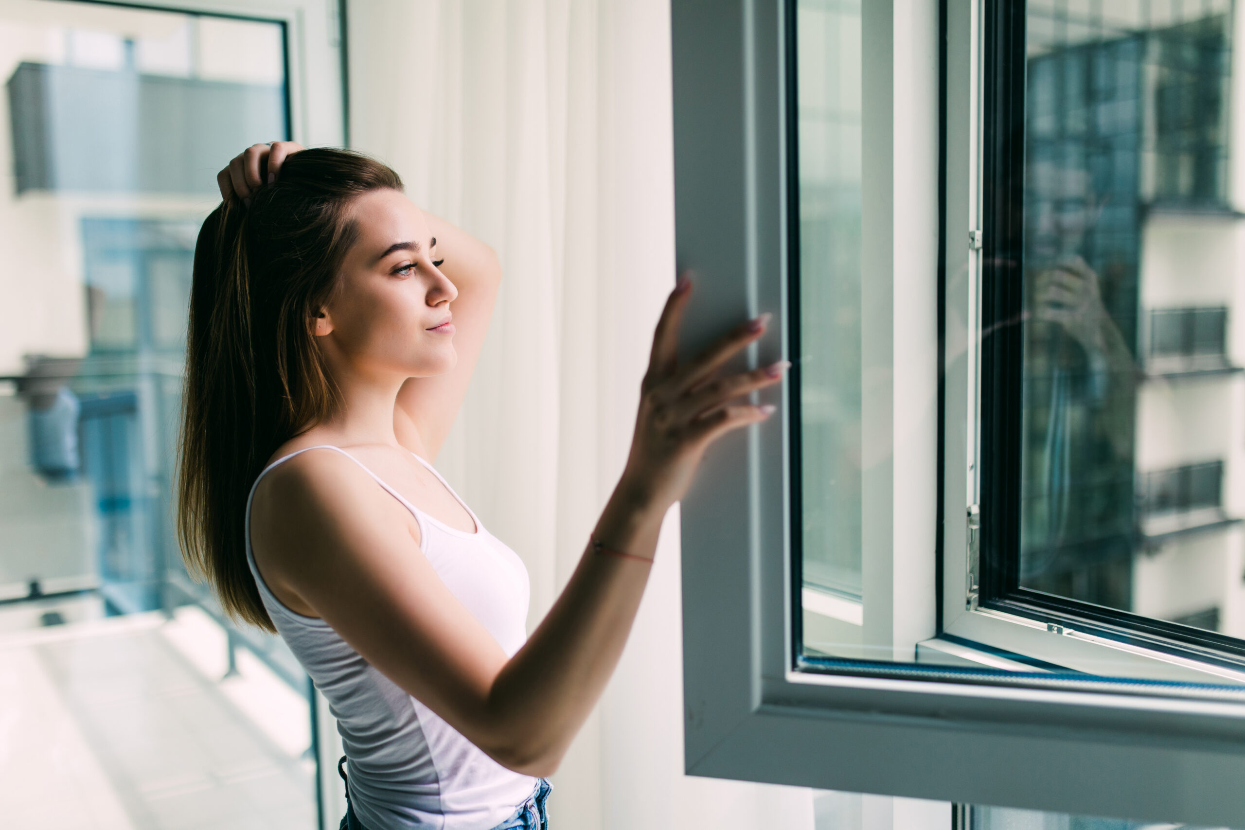 Young woman opens a plastic window for fresh air and smiling at home Woman opens a plastic window and smiling
